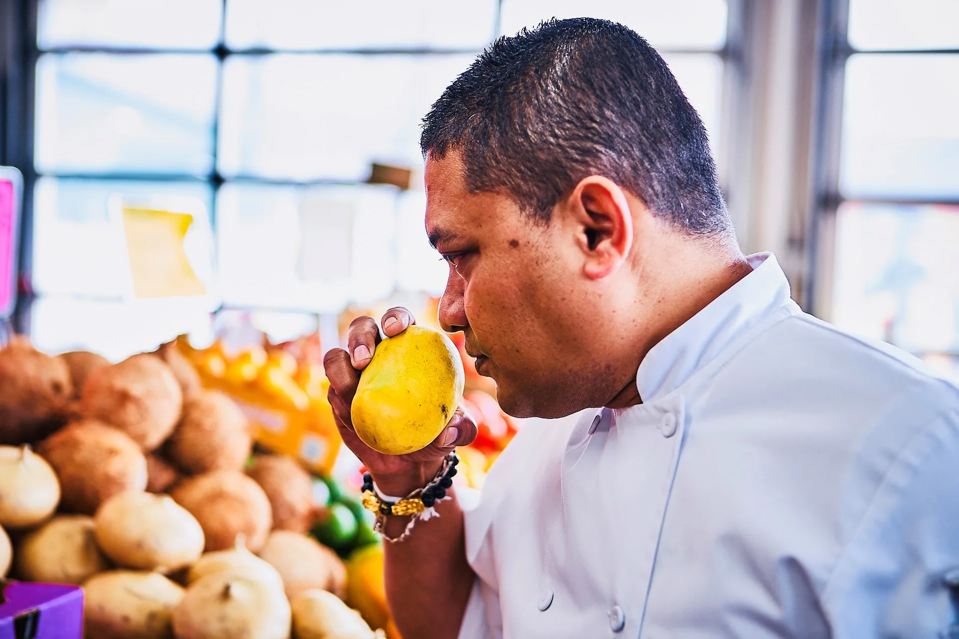 Chef Kal smelling a fresh mango at the market — sourcing the best ingredients for Taste of Pearl