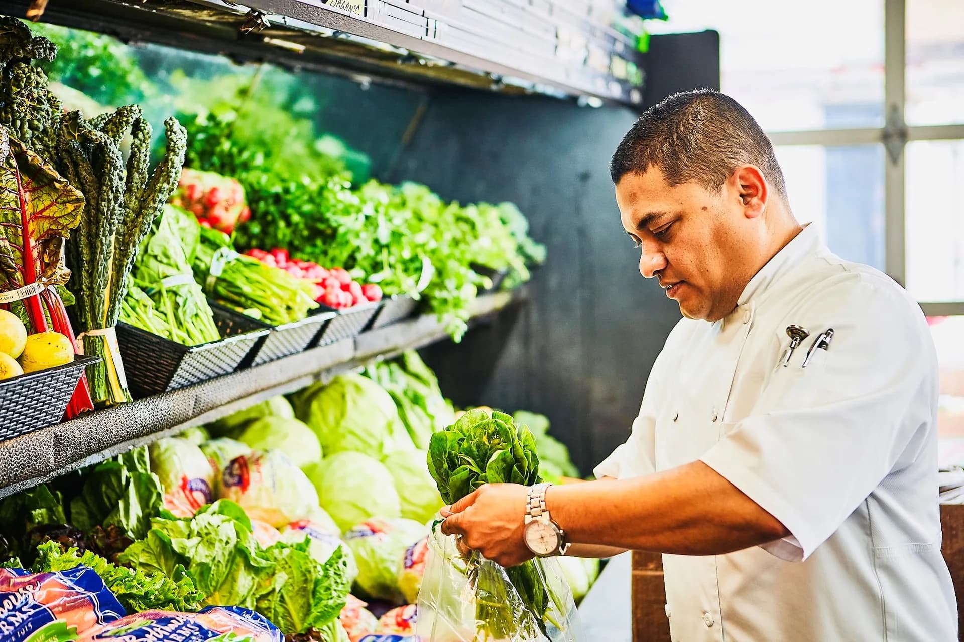 Chef Kal carefully selecting fresh greens at a local farmers market
